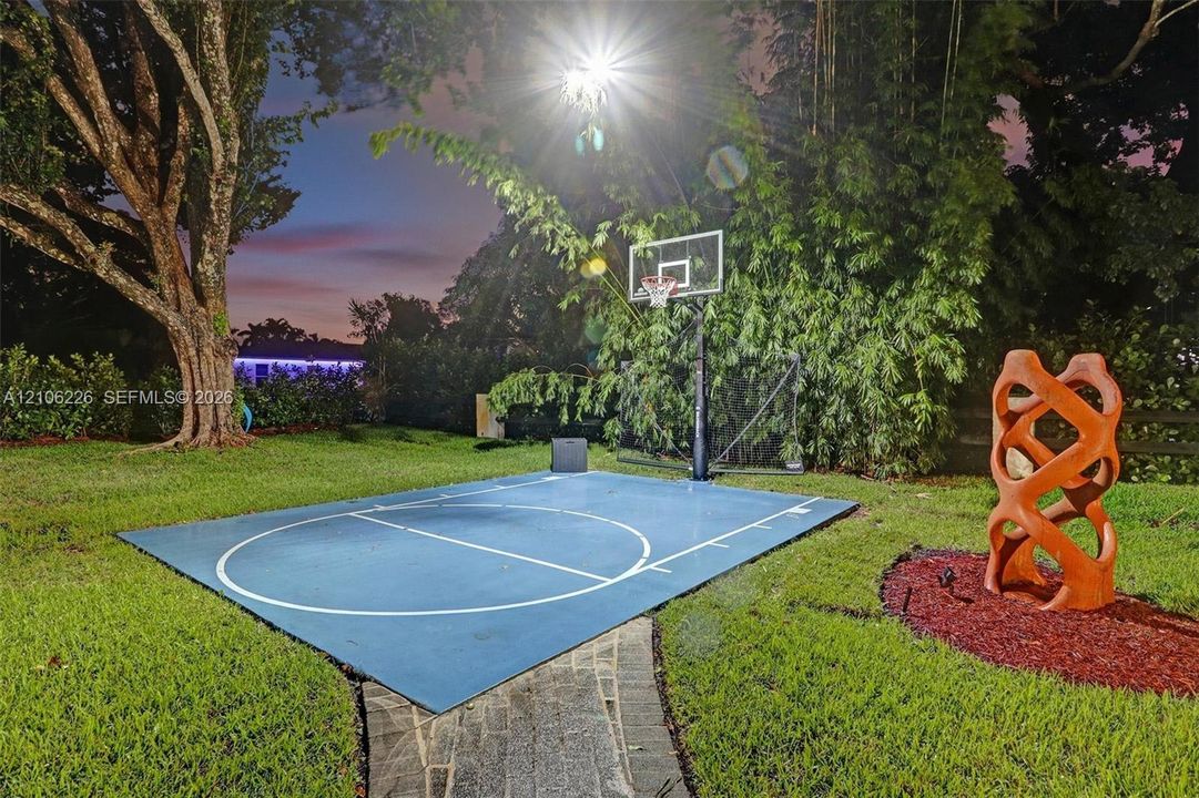 Backyard featuring a dedicated half-court basketball pad, stone pathway, and mature landscaping