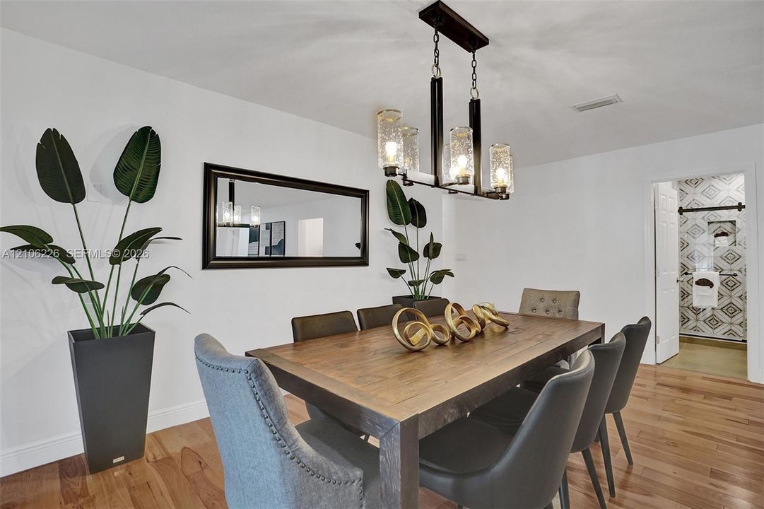 Dining area featuring wood-finish flooring, a rectangular wall-mounted mirror with a dark frame, and a four-light linear chandelier with textured glass shades
