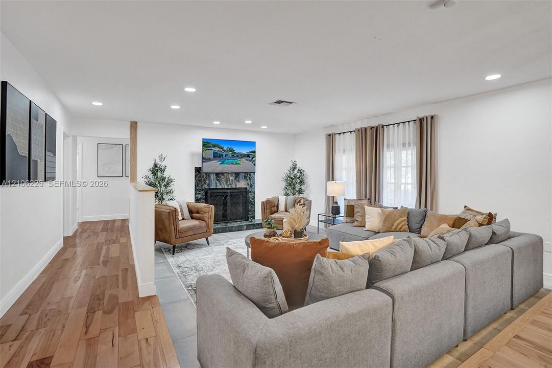Living area featuring wood-finish flooring, a full-height stone-surround fireplace, recessed ceiling lighting, and large windows with floor-to-ceiling drapery