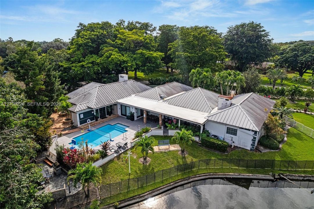 Metal roof residence featuring an in-ground swimming pool, covered patio, waterfront grounds, and mature landscaping
