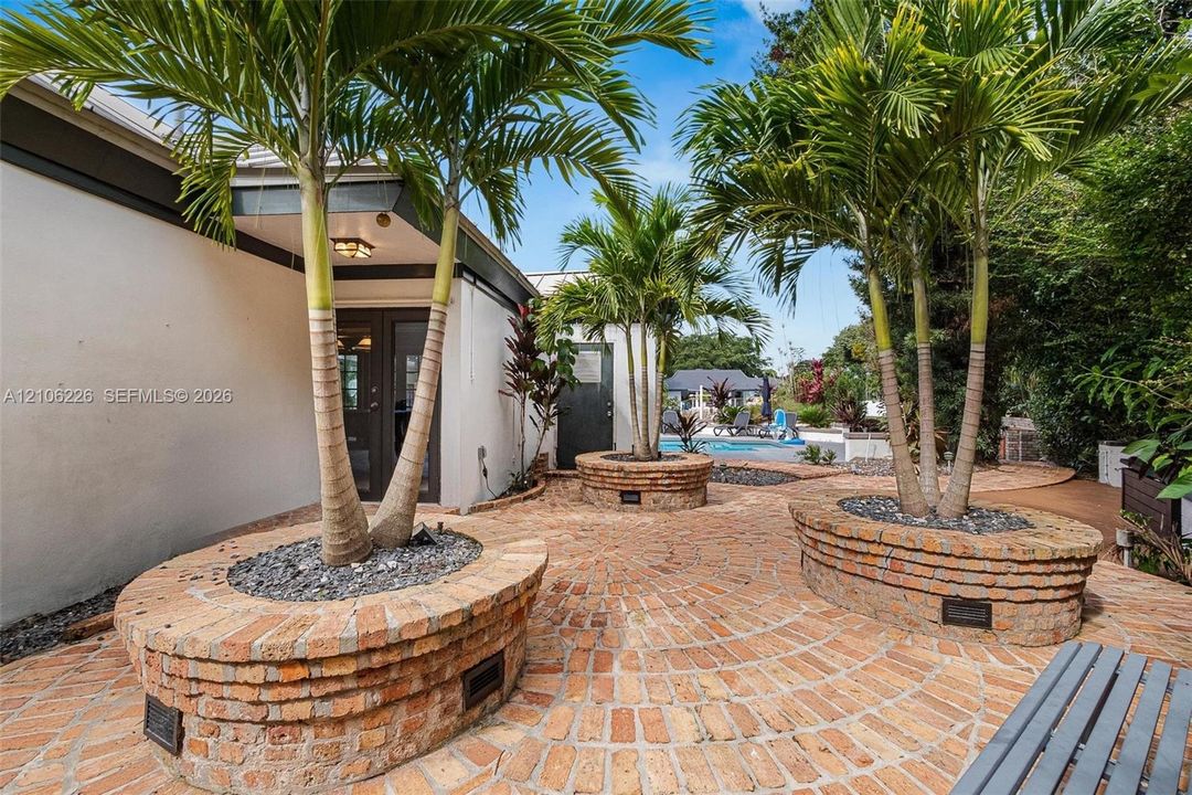 Exterior patio featuring a circular brick paver pattern, custom tiered brick planters, and mature palm trees