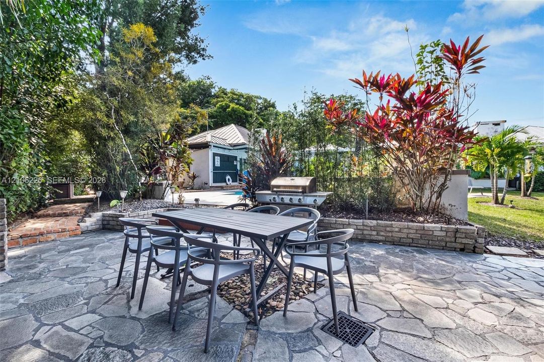 Flagstone patio featuring a built-in outdoor grill, raised brick planter beds, and lush tropical landscaping