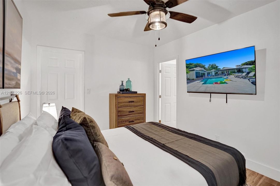 Neutral-toned bedroom featuring wood-finish flooring, a ceiling fan with integrated lighting, and multiple paneled doors