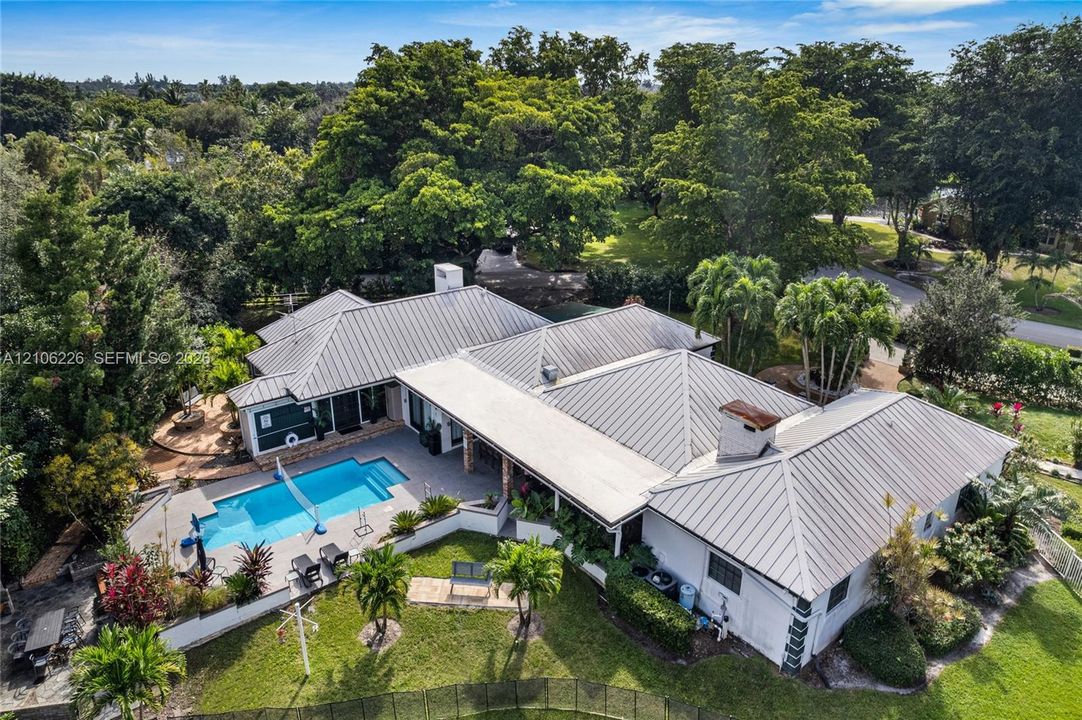 Metal-roofed residence featuring an inground swimming pool, paved patio, expansive lawn, and mature trees
