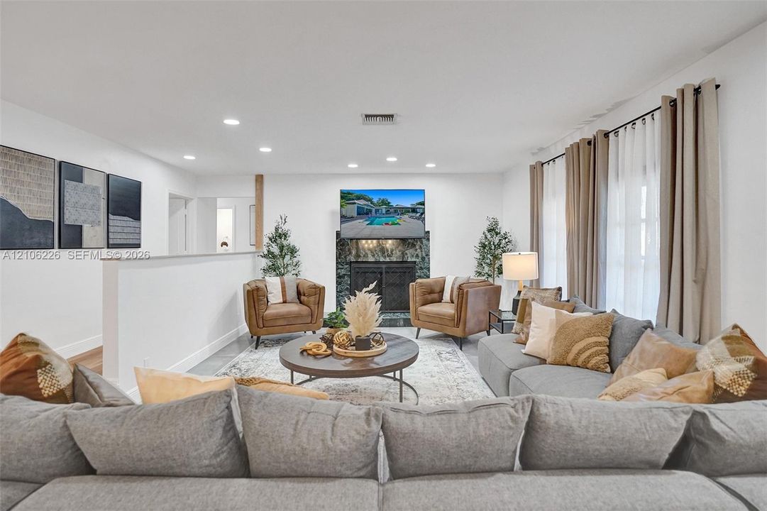 Spacious living area featuring recessed lighting, a fireplace with dark stone surround, and floor-to-ceiling windows