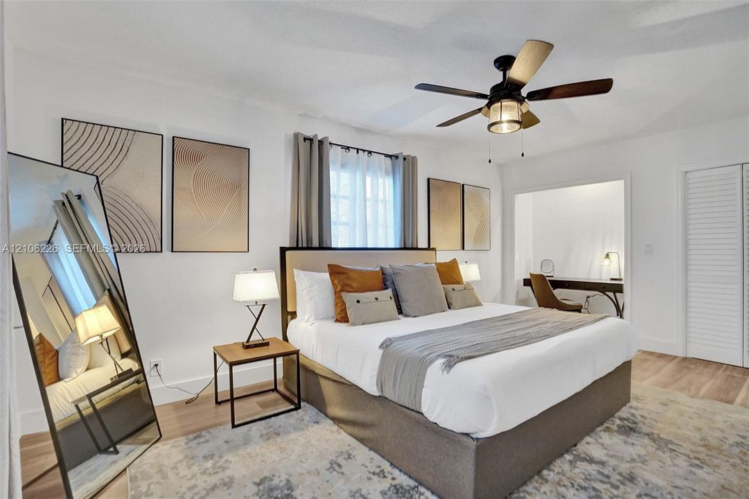 Bedroom featuring wood-finish flooring, multi-pane window, ceiling fan with integrated light fixture, and louvered closet doors