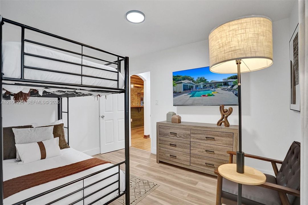 Neutral-toned room featuring wood-finish flooring, a flush-mount circular ceiling light, a white paneled door, and an arched entryway
