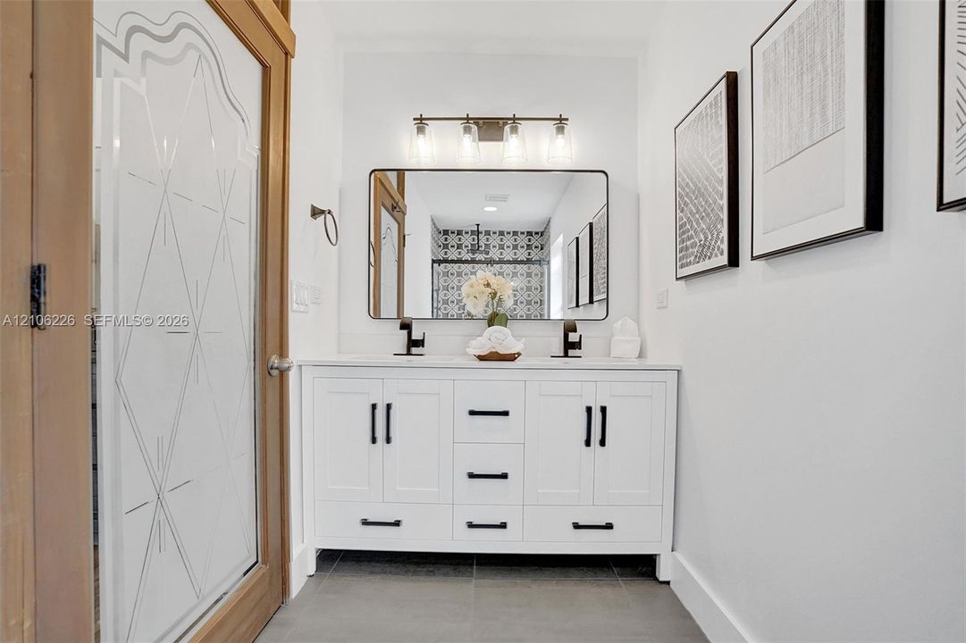 Double vanity featuring white cabinetry, black hardware, a rectangular framed mirror, three-light glass fixture, and dual faucets