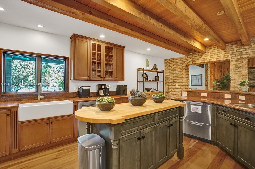 Kitchen featuring an exposed wood beam ceiling, brick accent wall, white farmhouse sink, butcher block island countertop, and custom wood cabinetry