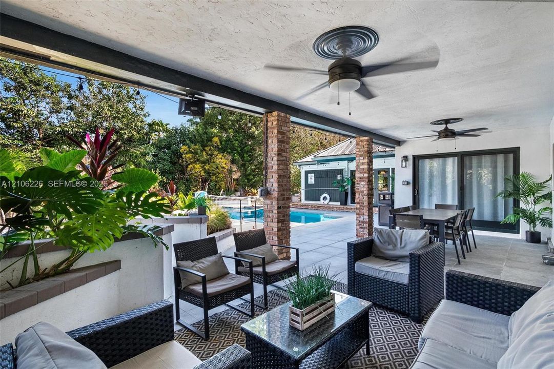Covered patio featuring exposed brick columns, concrete tile flooring, dual ceiling fans, and integrated lighting