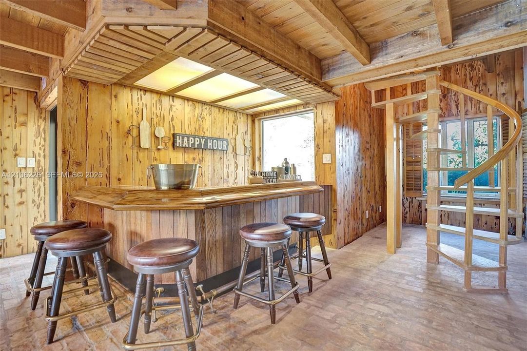 Custom built-in wood bar featuring recessed lighting, paneled wood walls, wood beam ceiling, and a spiral staircase