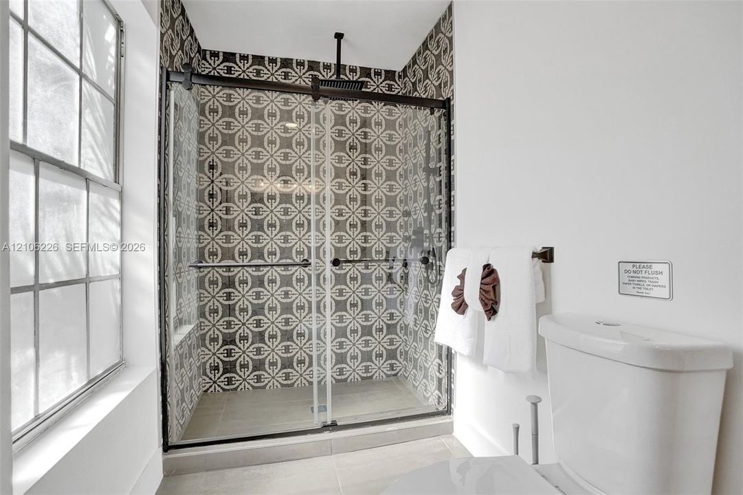 Walk-in shower featuring patterned tile walls, sliding glass enclosure, matte black hardware, and an overhead rain showerhead