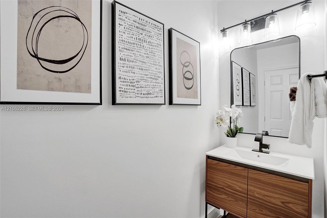 Vanity with a wood-finish cabinet, integrated rectangular sink, matte black faucet, and a rectangular mirror with a matching black frame, illuminated by a multi-bulb light fixture