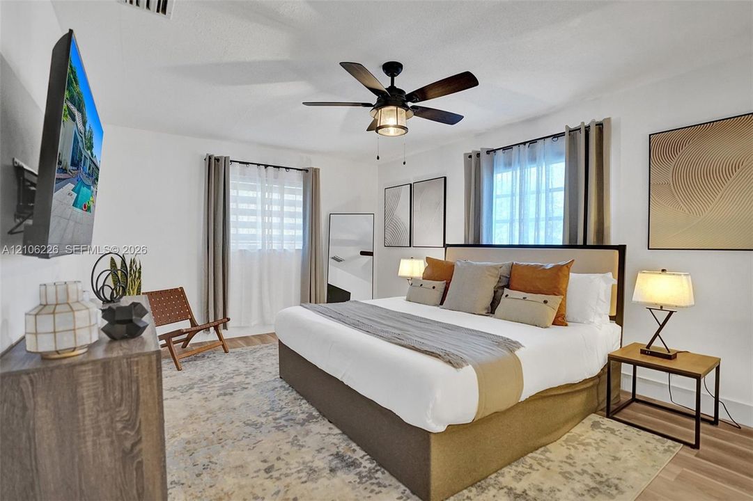 Neutral-toned interior featuring wood-finish flooring, a multi-blade ceiling fan with integrated lighting, and dual windows with window treatments
