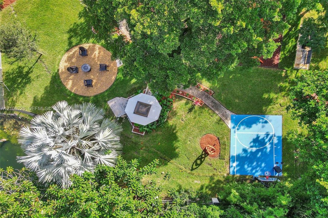 Expansive grounds featuring a dedicated basketball court, a custom gazebo, a circular mulched gathering area, and mature landscaping
