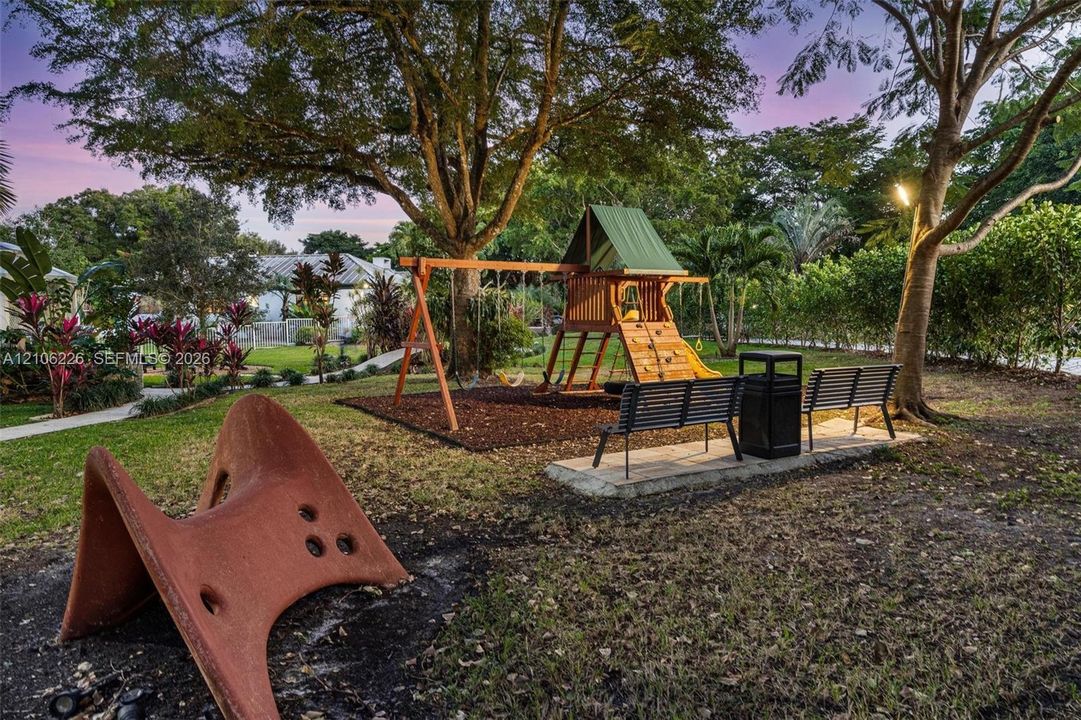 Expansive outdoor grounds featuring a wooden play structure, mature trees, manicured landscaping, paved walkways, and metal bench seating