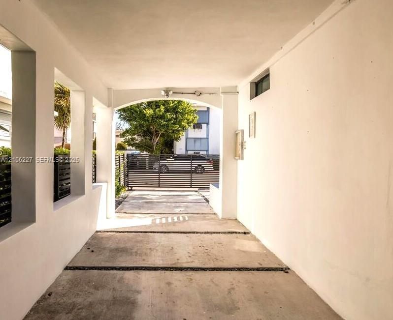 Covered carport featuring an arched entryway, smooth stucco finish, concrete slab flooring, and a metal security gate