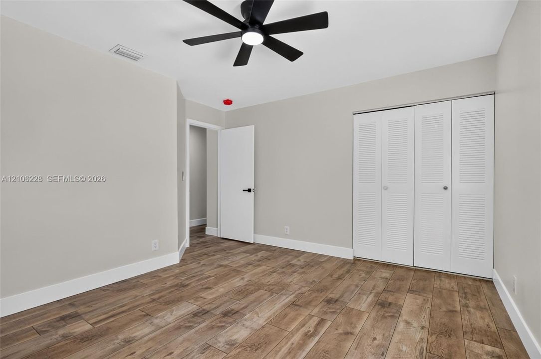 Wood-finish flooring, matte black ceiling fan with integrated lighting, and white louvered-door closet