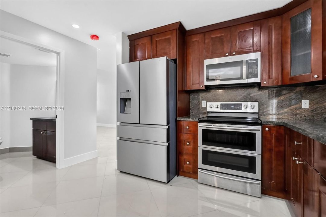 Kitchen featuring dark wood-finish cabinetry, stone backsplash, stainless steel appliances, and large-format tile flooring