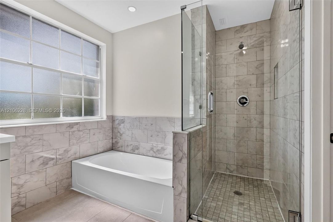 Bathroom featuring a deep soaking tub, separate glass-enclosed shower with a recessed niche, stone-patterned wall tile, frosted window, and brushed-nickel hardware
