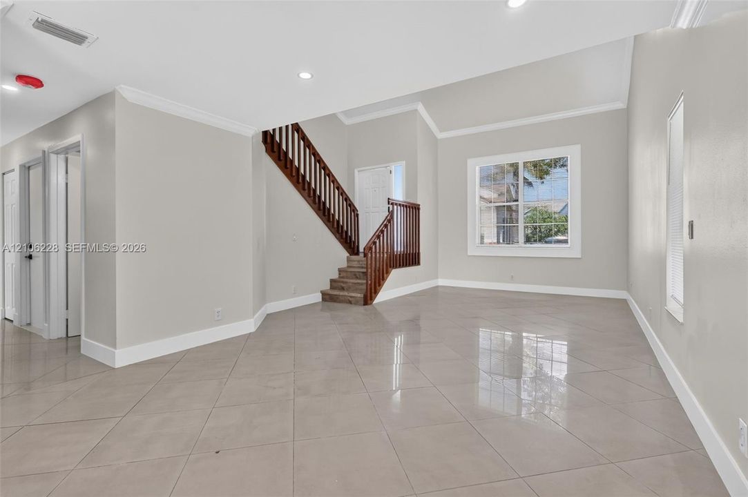 High-ceilinged room featuring large-format ceramic tile flooring, a staircase with a dark wood-finish balustrade, crown molding, and recessed lighting