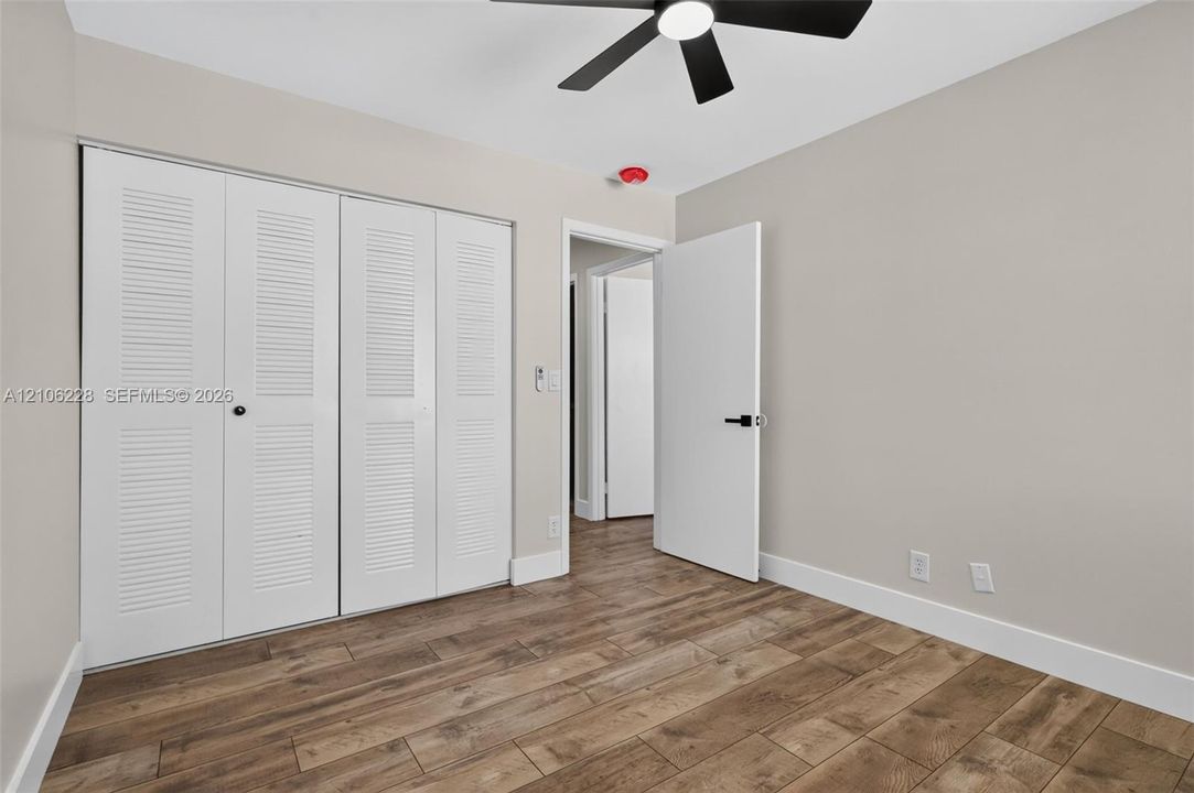 Wood-finish flooring, white louvered-door closet, and modern black ceiling fan with integrated lighting