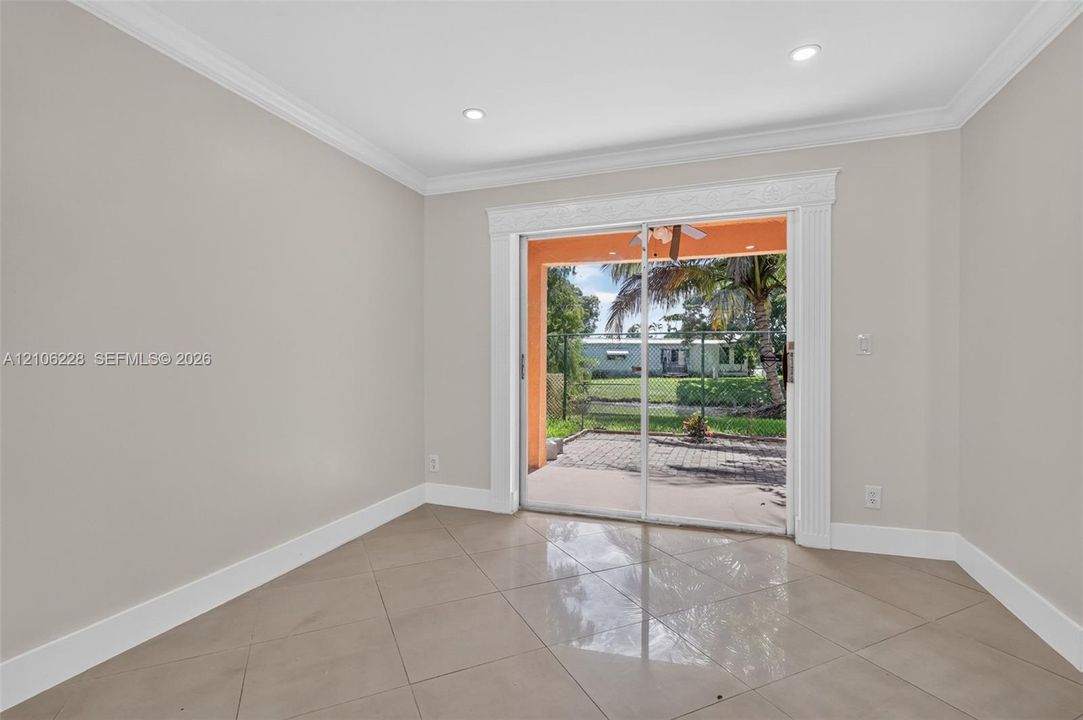 Neutral interior featuring large-format ceramic tile flooring, recessed ceiling lighting, crown molding, and sliding glass doors with decorative casing