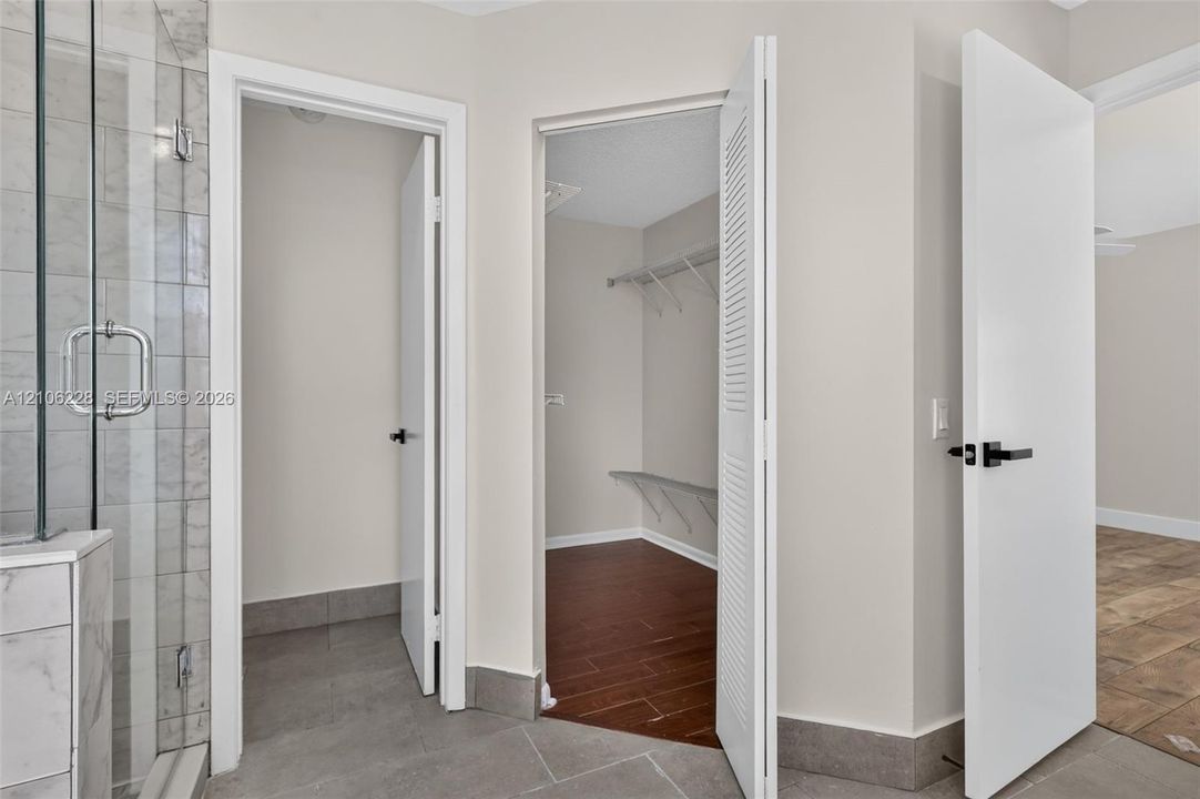 Glass-enclosed shower with tiled surround, walk-in closet featuring wire shelving, wood-finish flooring, and minimalist doors with matte black hardware