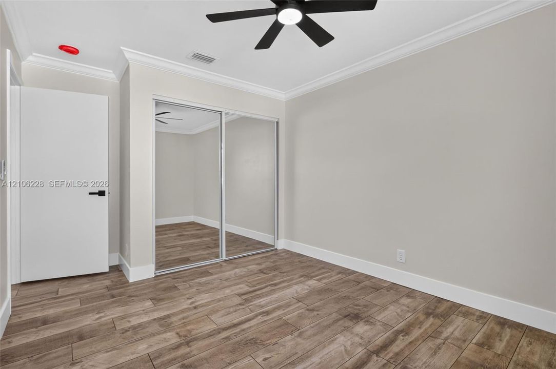 Room featuring wood-finish flooring, crown molding, a ceiling fan, and sliding mirrored closet doors