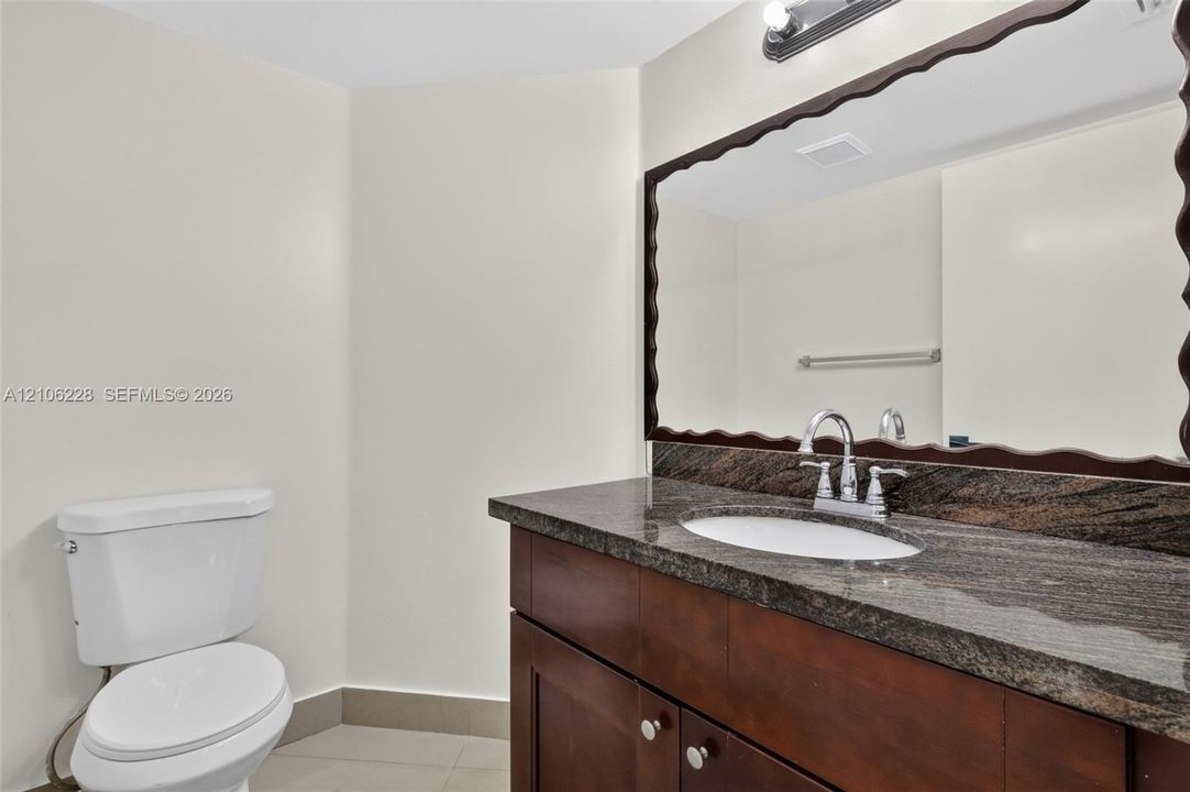 Dark wood-finish cabinetry with a stone-top vanity, undermount sink, dual-handle faucet, and decorative-edge wall mirror