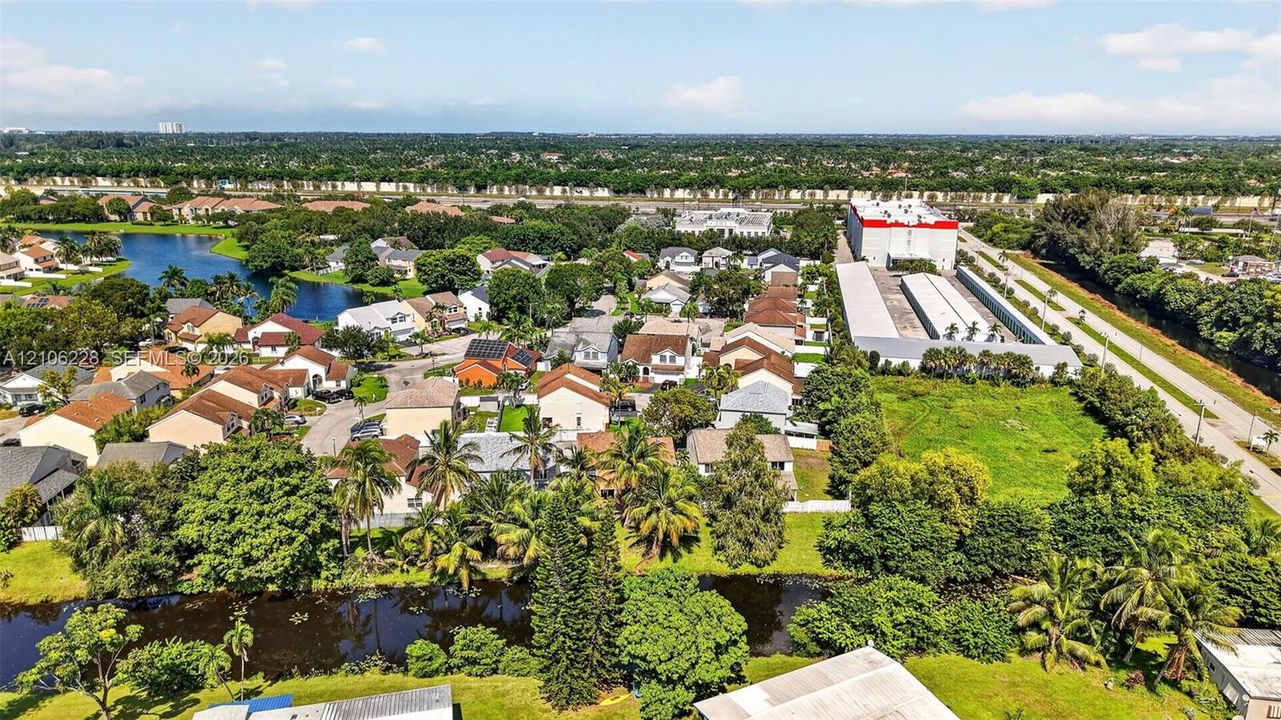 Aerial perspective of the residential area featuring a canal, mature trees, dense greenery, and proximity to regional infrastructure