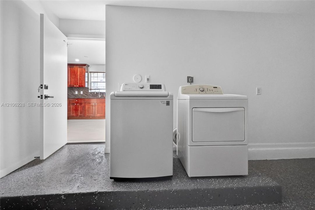 Laundry area featuring a raised platform, white walls, and speckled concrete-finish flooring