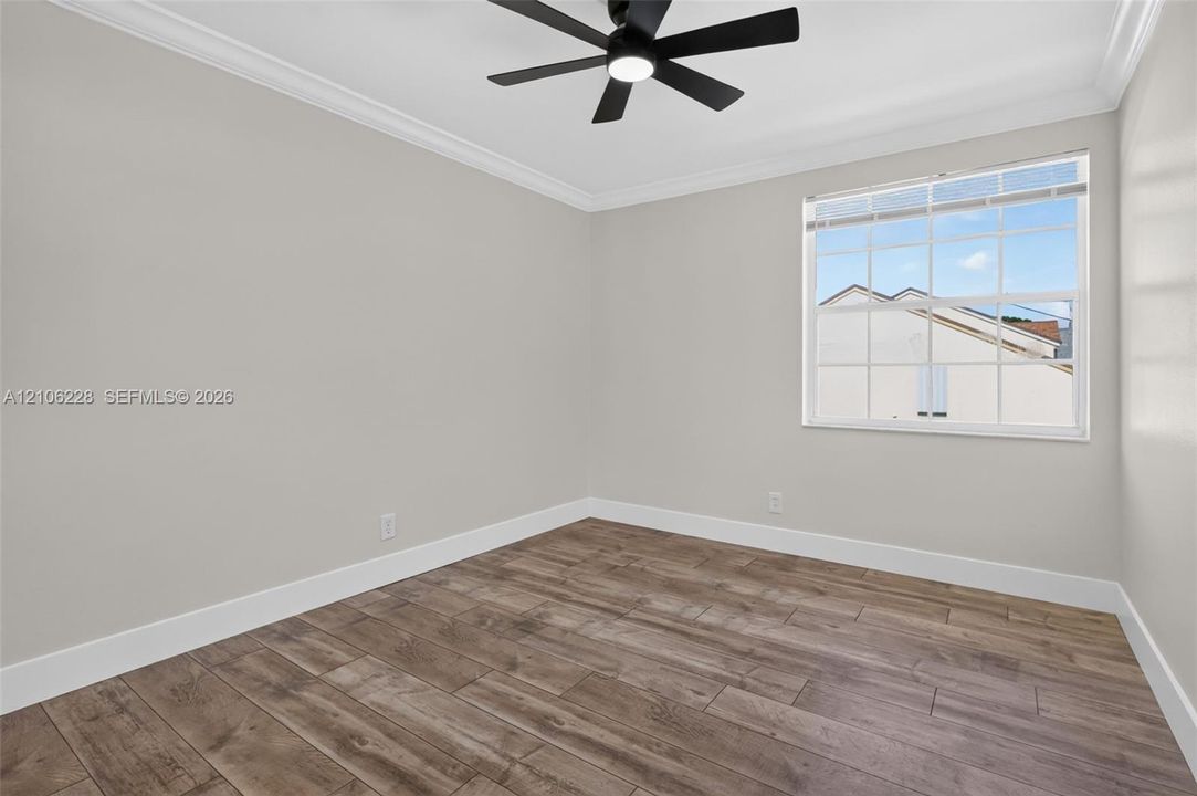 Interior space featuring wood-finish flooring, neutral wall paint, crown molding, multi-pane window, and a matte black ceiling fan