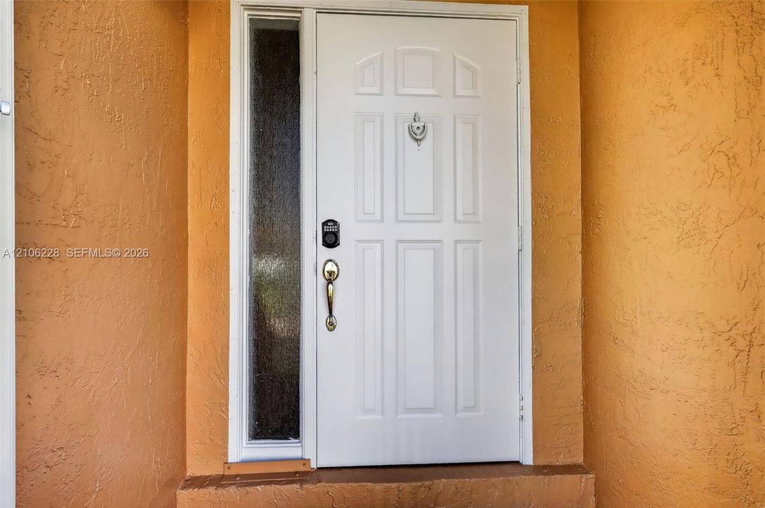 Entry door featuring a white six-panel design, textured stucco exterior wall, sidelight with privacy glass, metallic hardware, and door knocker