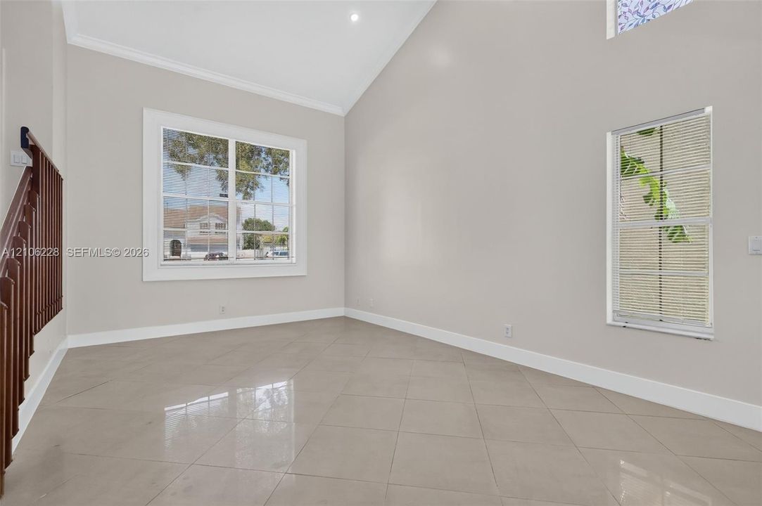 Vaulted ceilings, large multi-pane windows, polished tile flooring, and dark-stained wooden staircase railing