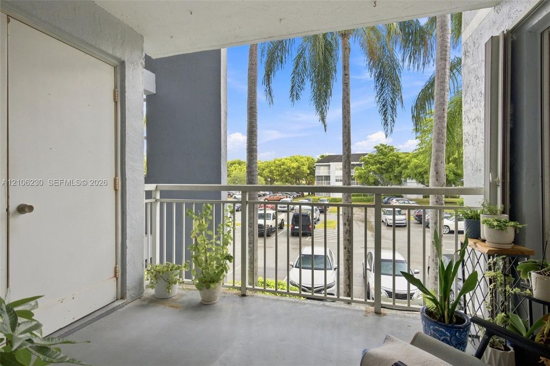 Covered balcony featuring concrete flooring, white metal railing, and a private entry door