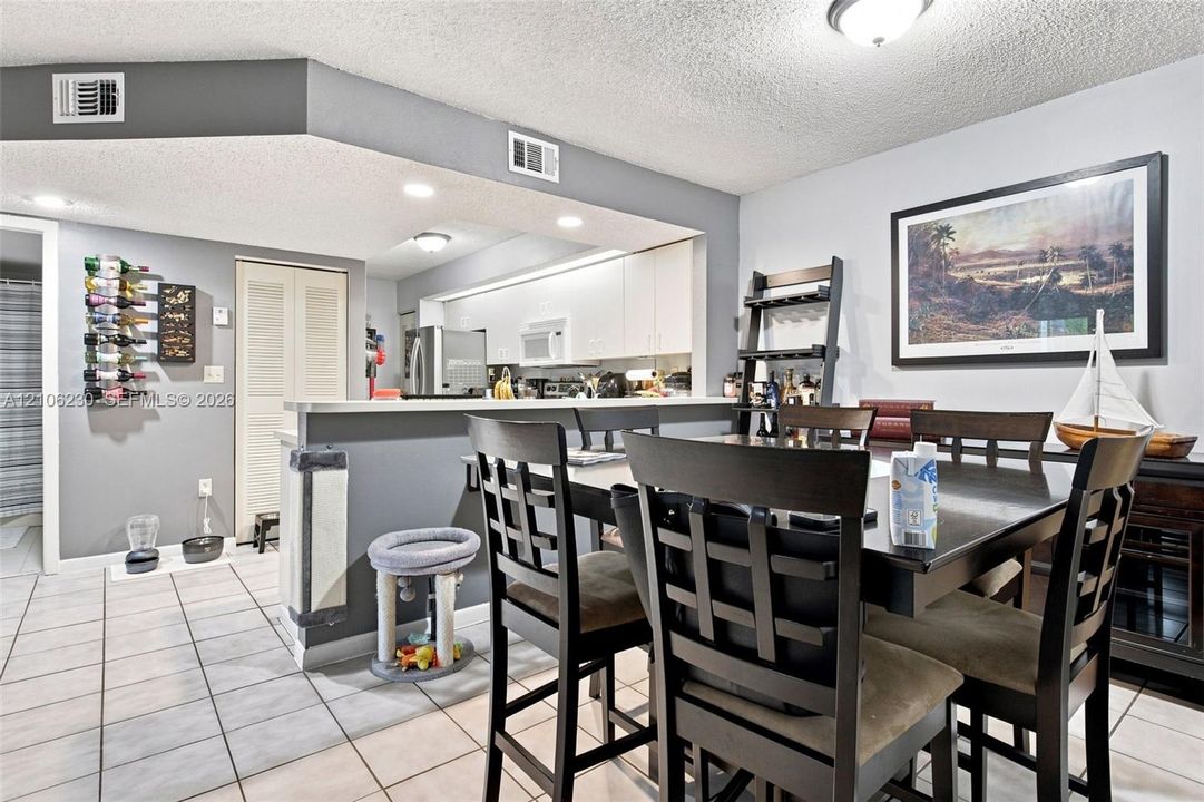 Open-concept interior featuring light-colored ceramic tile flooring, a breakfast bar with stone-finish countertop, recessed ceiling lighting, and crisp white cabinetry