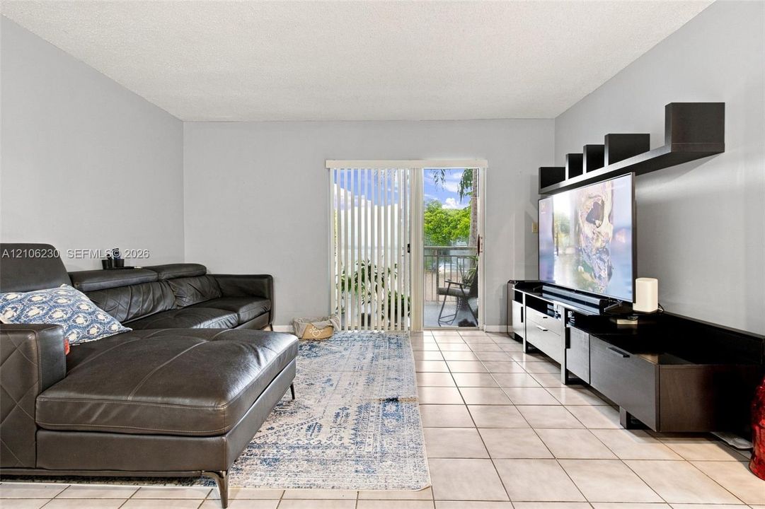 Living area featuring large format tile flooring and a sliding glass door with vertical blinds