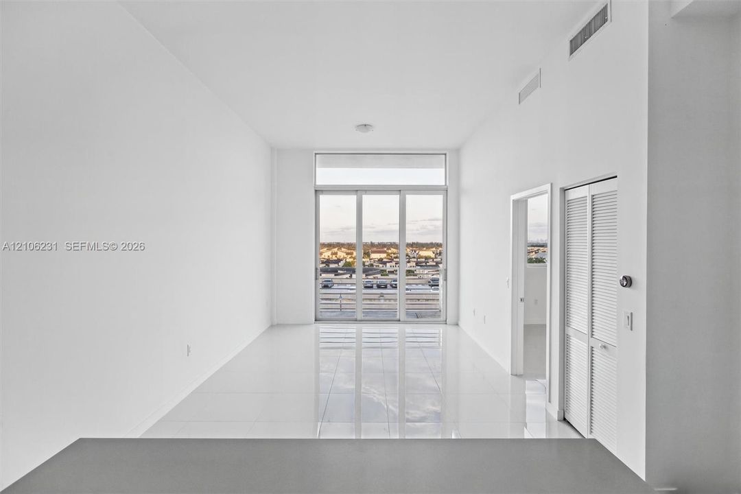 Living area features high ceilings & full-height glass sliding doors, polished tile flooring, and louvered bifold closet doors