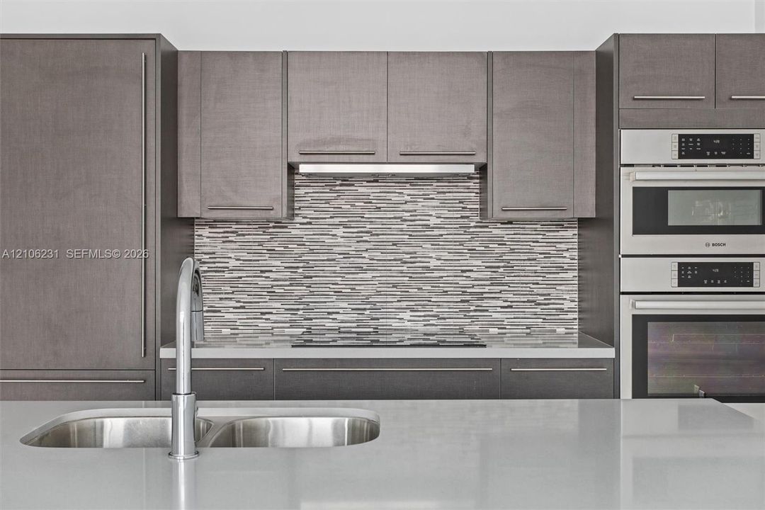 Modern kitchen featuring flat-panel cabinetry, quartz countertops, a mosaic tile backsplash, integrated stainless steel appliances, and a double-basin undermount sink with a gooseneck faucet