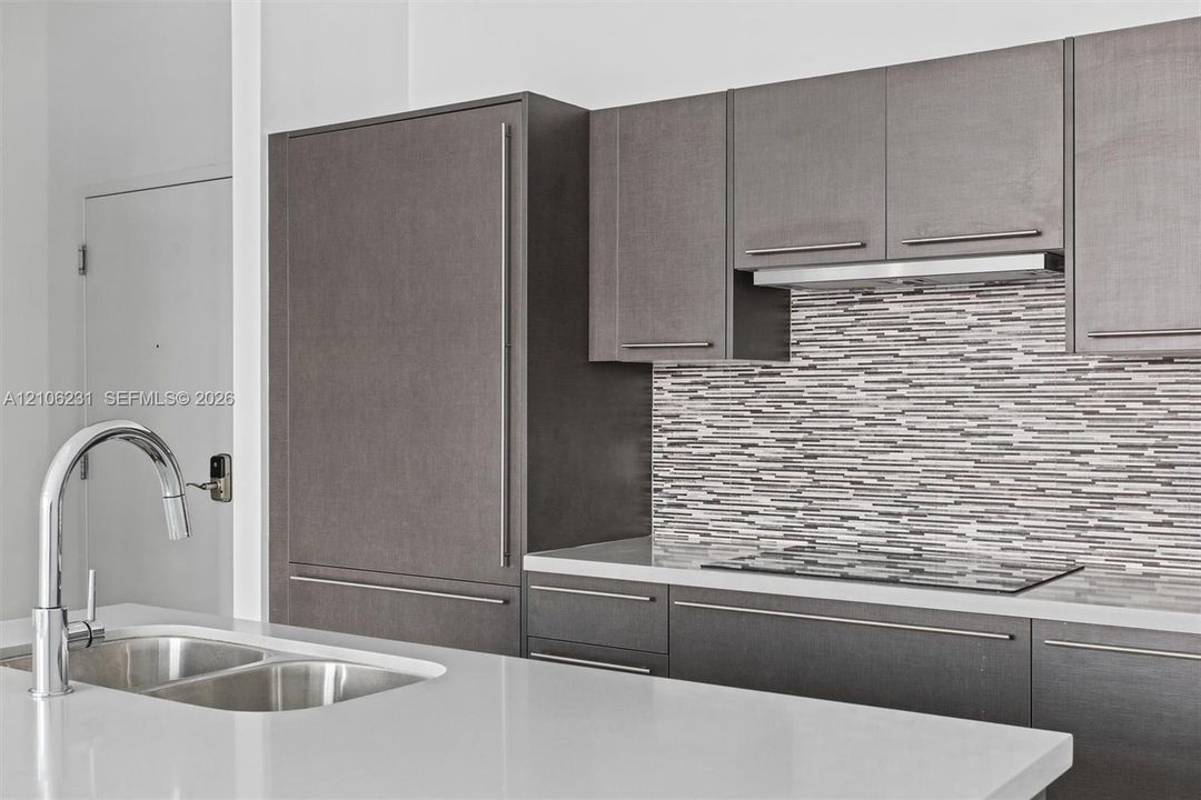 Kitchen featuring flat-panel cabinetry, quartz countertops, horizontal mosaic tile backsplash, integrated Bosch refrigerator, and stainless steel undermount double-basin sink with arched pull-down faucet