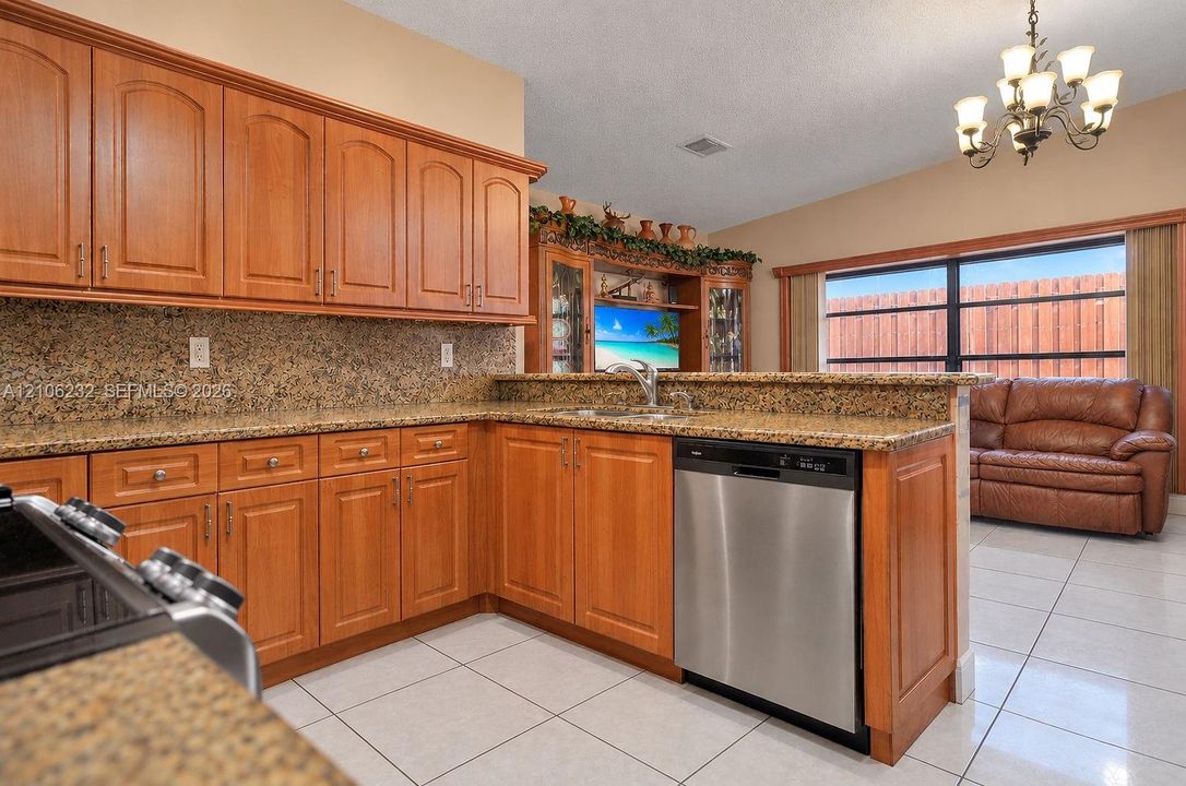 Kitchen featuring natural wood cabinetry, stone-surface countertops, built-in cabinetry, stainless steel dishwasher, and a chandelier
