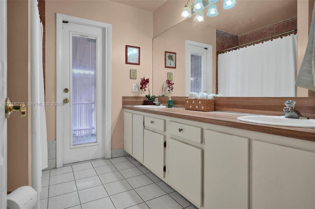 Dual vanity featuring white cabinetry, integrated sinks, a wood-finish countertop, full-width wall mirror, and ceramic tile flooring