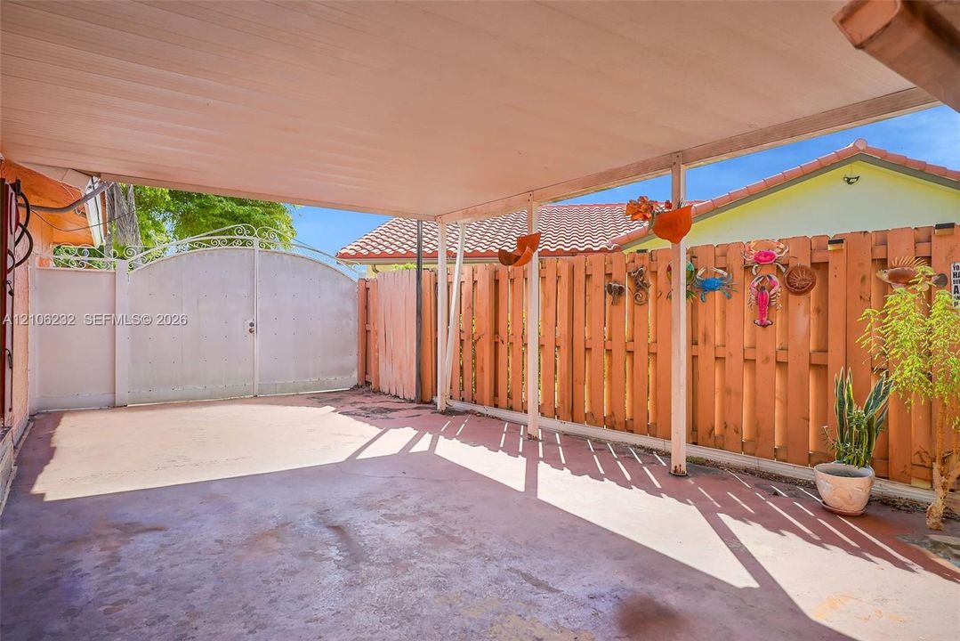 Covered concrete patio featuring a perimeter wood-slat privacy fence and a solid-panel arched metal gate