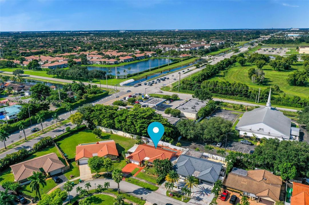 Aerial perspective featuring a tile-roofed residence with a multi-car garage, established landscaping, and perimeter fencing within a suburban setting