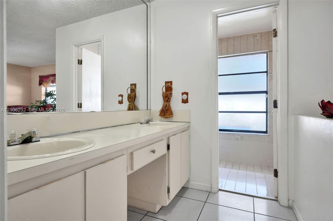 Bathroom vanity featuring a solid-surface countertop, dual drop-in basins, extensive wall-to-wall mirror, and neutral cabinetry