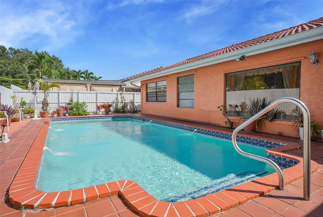 In-ground swimming pool with built-in water features, terracotta-style tiled patio, and privacy fencing