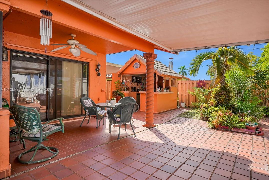 Covered patio featuring terra cotta tile flooring, a built-in outdoor bar with a tile-roofed structure, a decorative spiral column, and mature landscaping