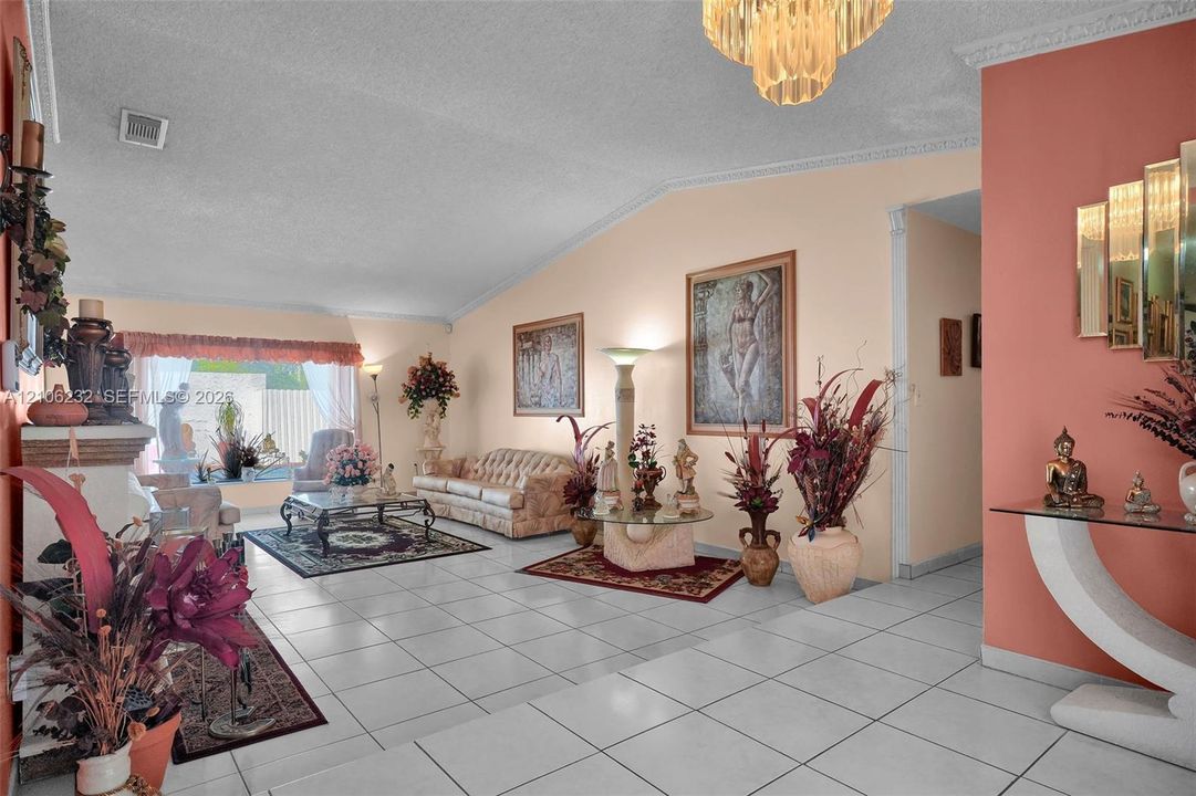 Vaulted ceiling with decorative crown molding and an integrated chandelier, complemented by neutral tile flooring