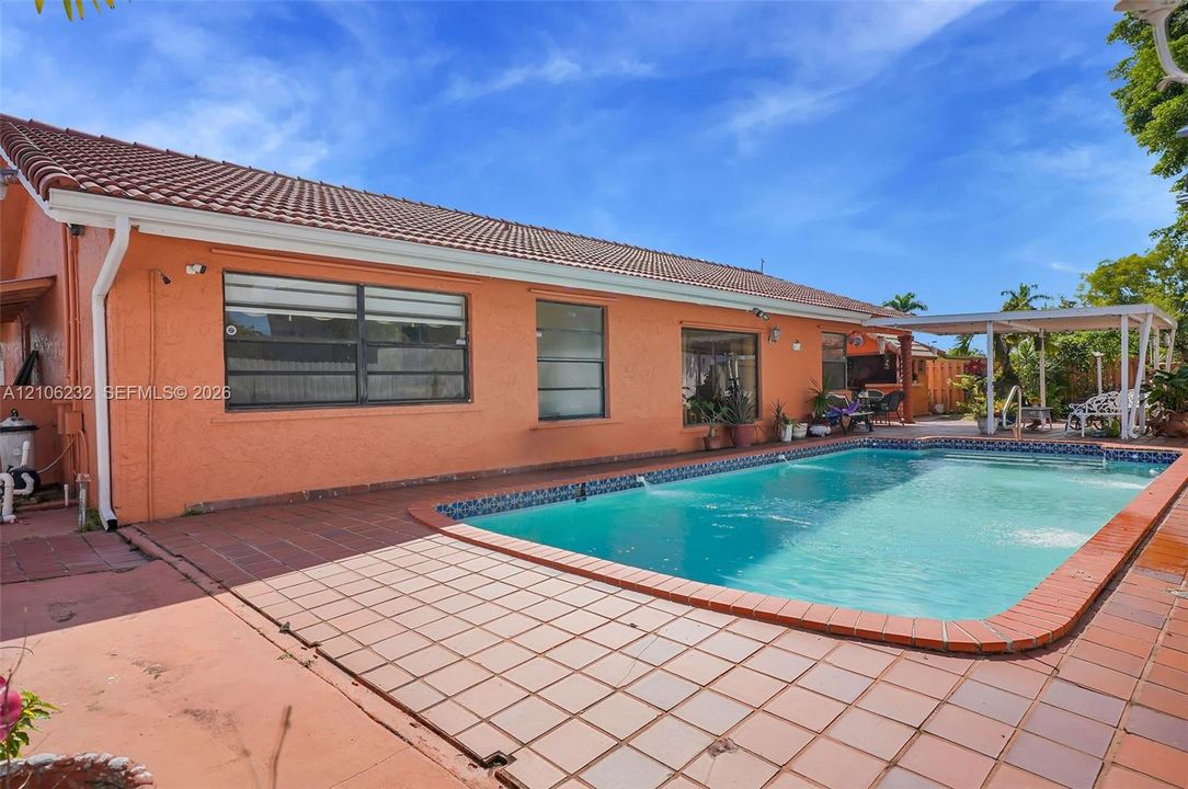 Stucco exterior featuring a tile roof, an in-ground pool with tile coping, and a covered patio area